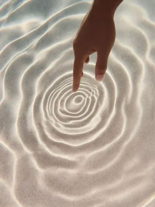 A fingertip touching still water, sending out slow ripples