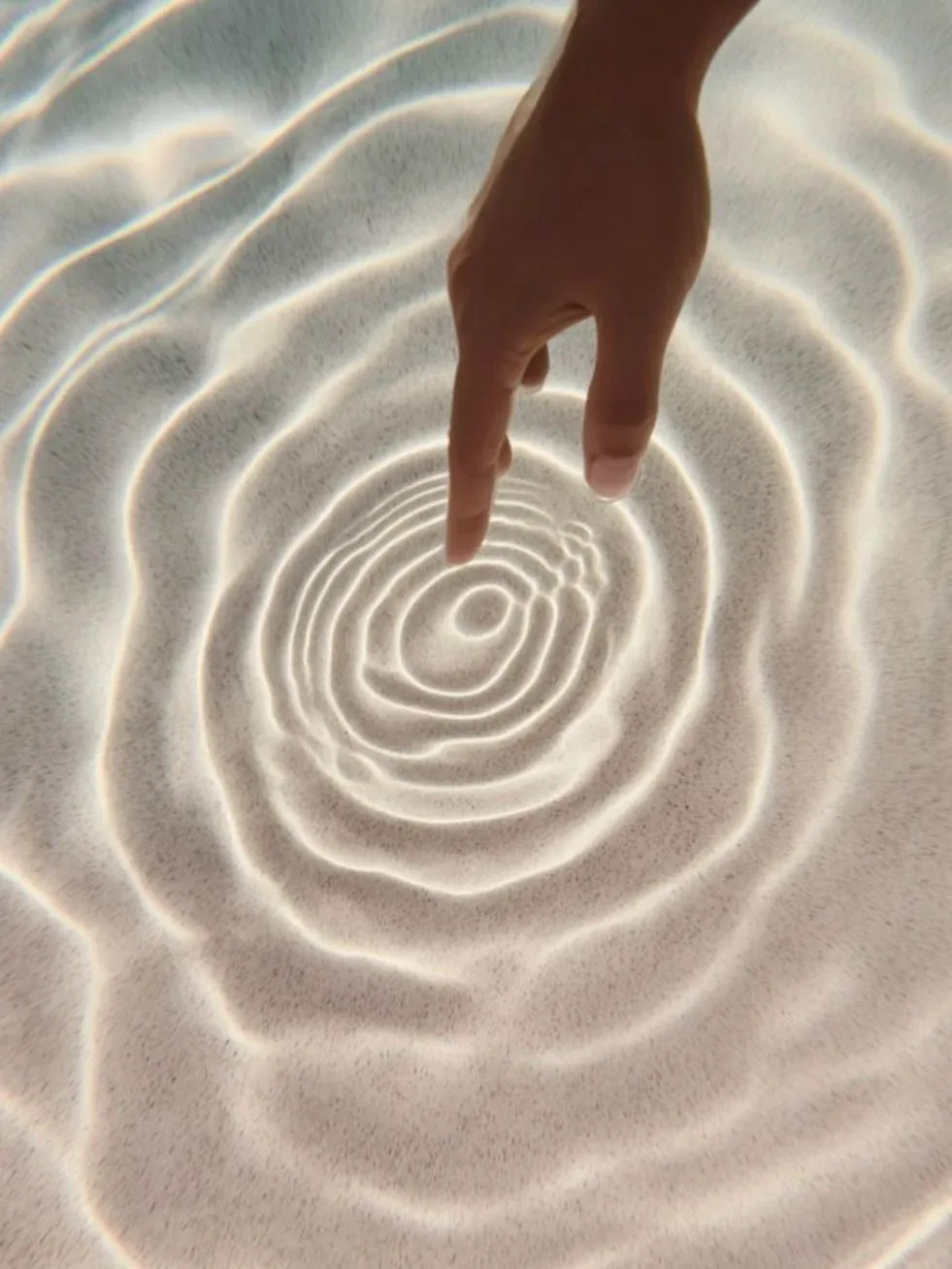 A fingertip touching still water, sending out slow ripples