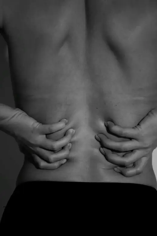 A woman's lower back held with both hands, soft black and white