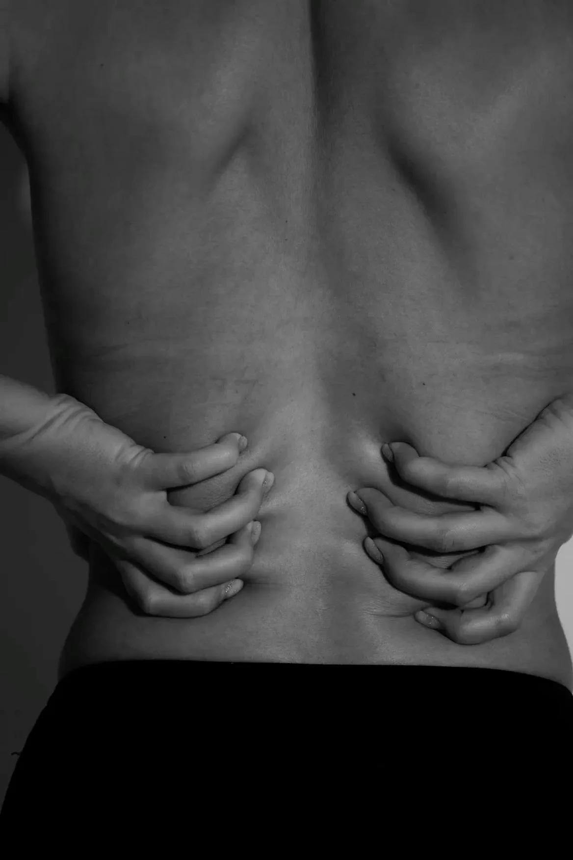 A woman's lower back held with both hands, soft black and white